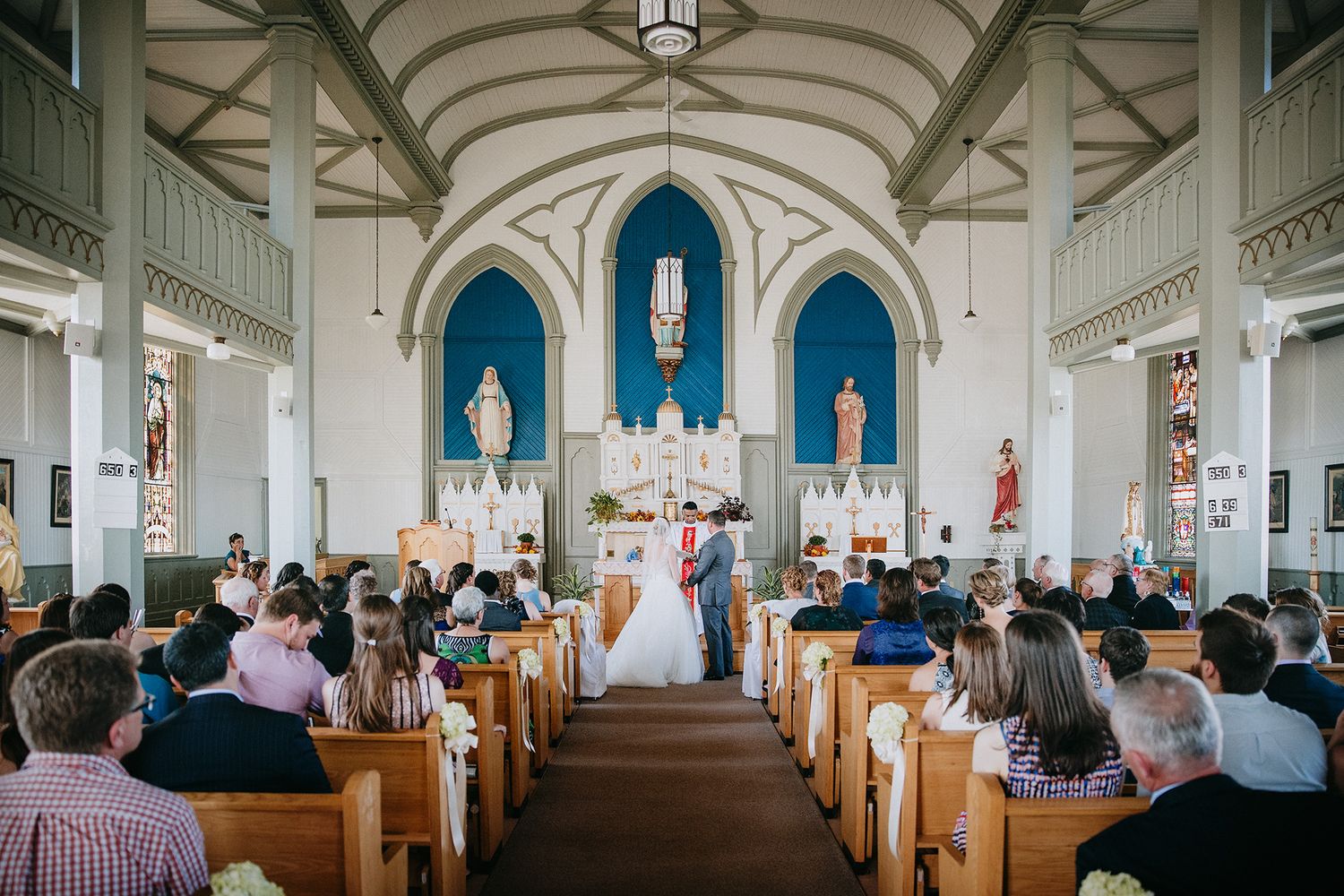 Interior panorama of a traditional church sanctuary with wooden pews and vaulted ceiling during a wedding.