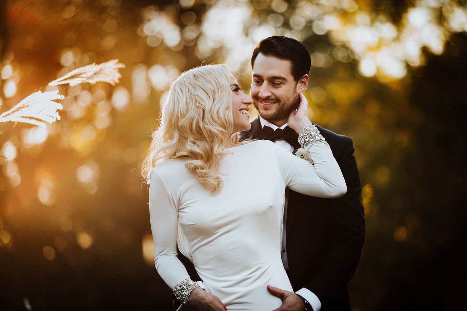 A couple shares an intimate moment at sunset with golden light filtering through trees in the background.