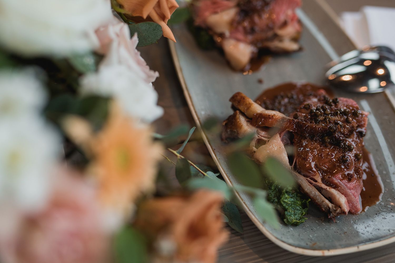 Family-style beef dish with floral bouquet in foreground.