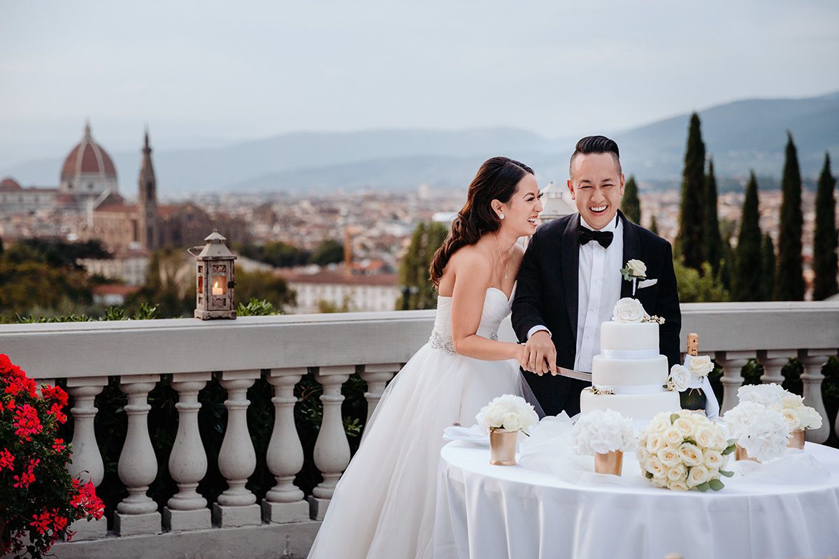 A wedding couple cut their wedding cake at an outdoor reception overlooking Florence, Italy with the Duomo in view.