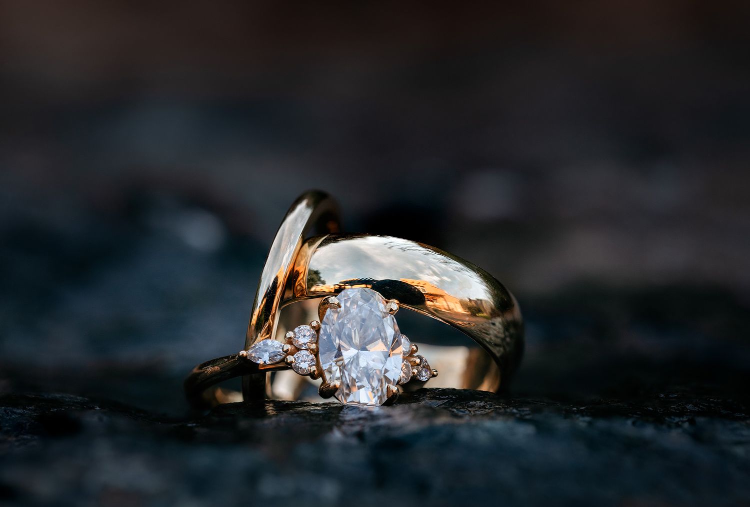 Close-up of gold wedding rings with diamond solitaire on dark textured surface with soft lighting.