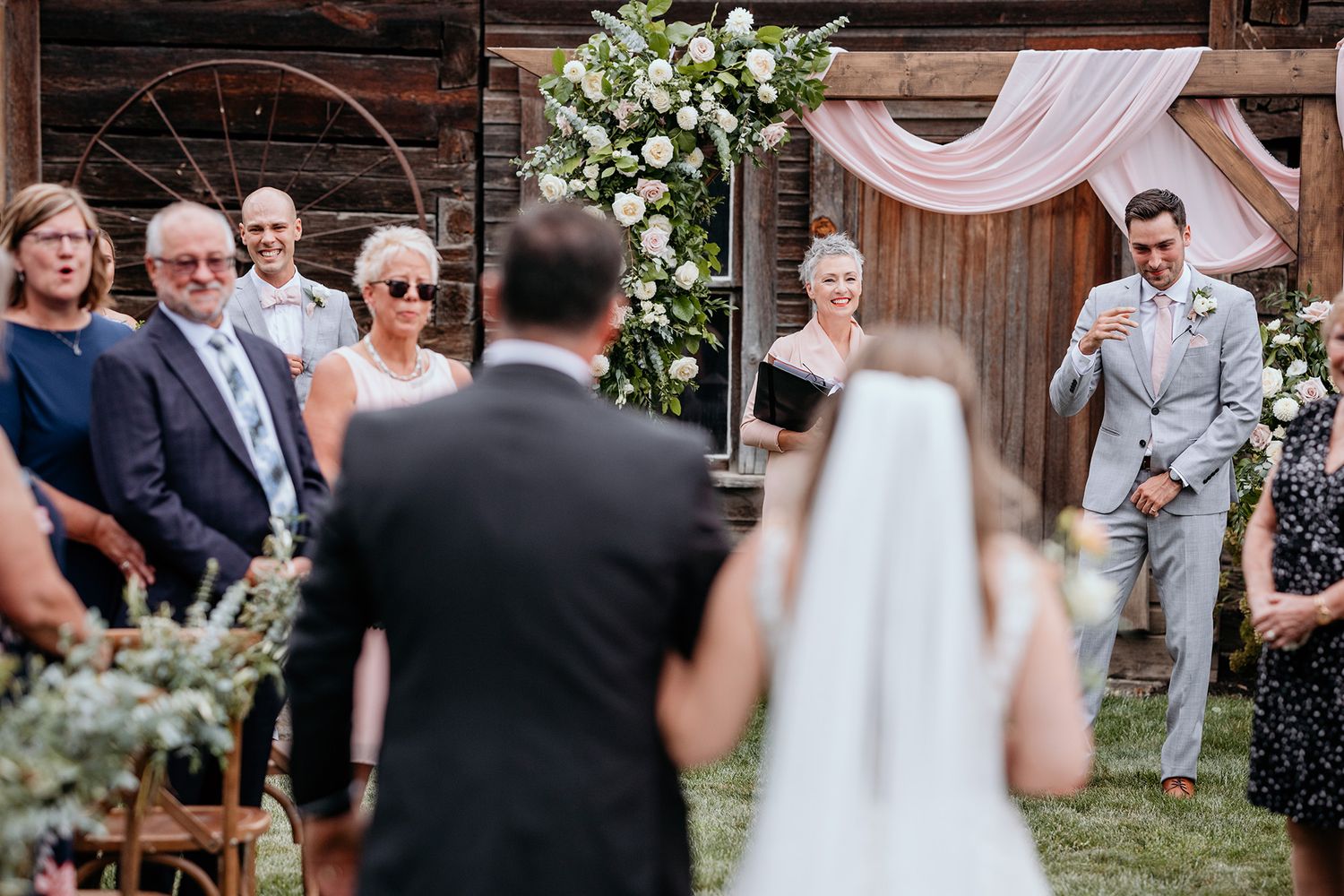 An emotional groom anticipates his bride's arrival at a rustic barn wedding with string lights, floral arrangements.