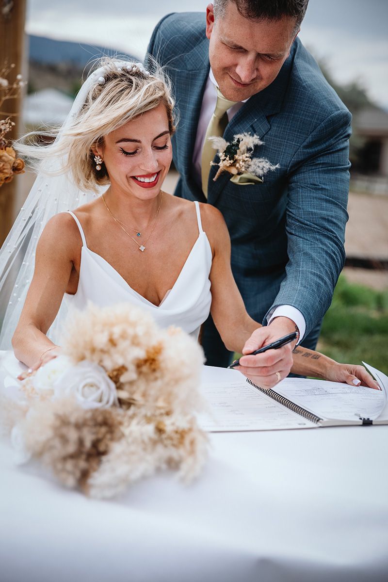 Close-up shots of a bride and groom signing their marriage license at an outdoor wedding ceremony.