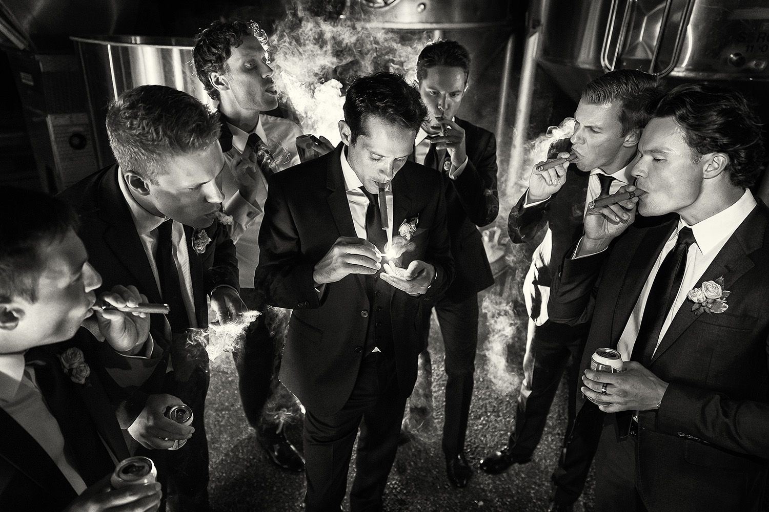 Black and white image of a groom and his groom's men enjoy cigars among the vats of Summerhill Pyramid Winery in Kelowna.