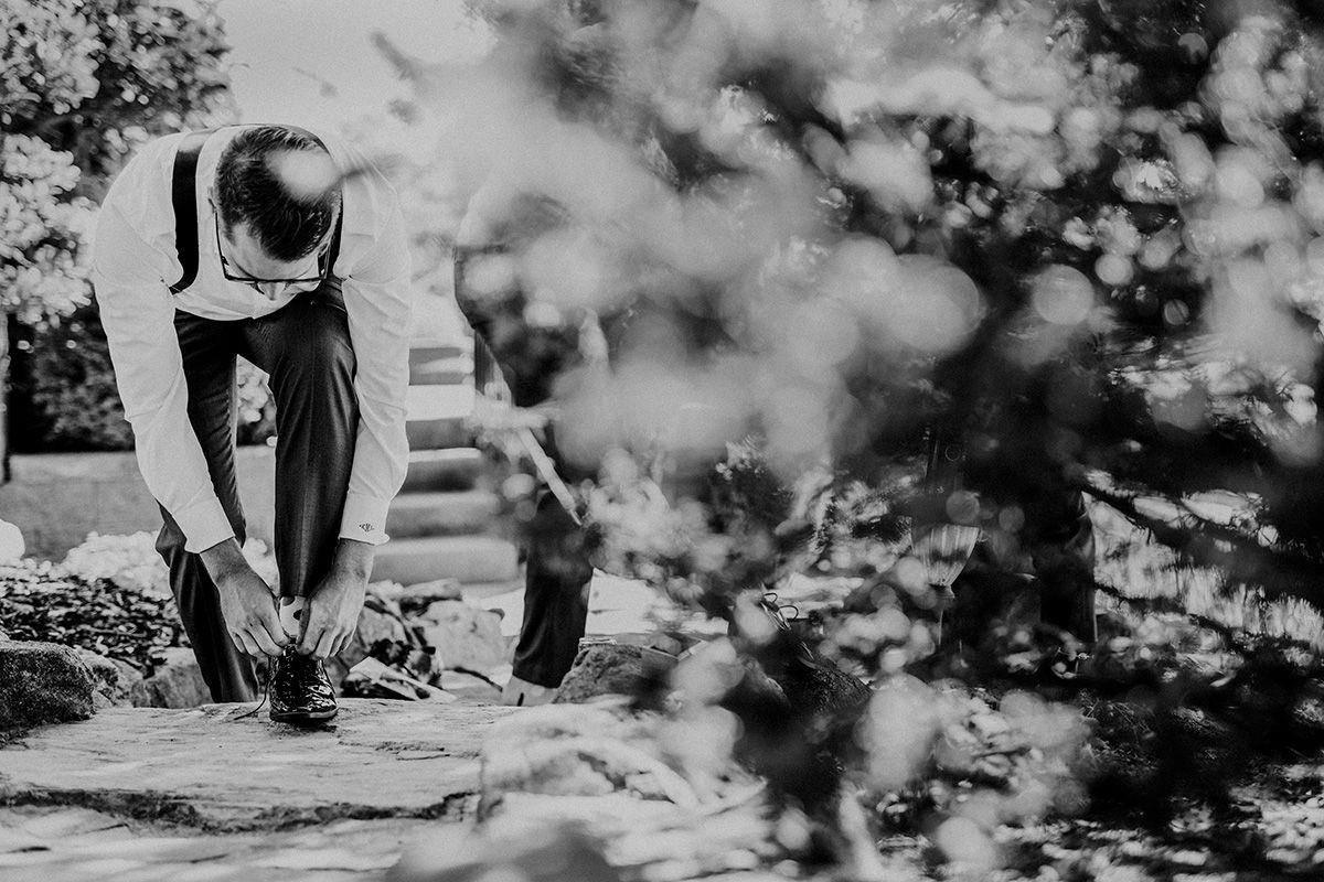 A black and white artistic photo showing a well-dressed man bending down to tie his shoe on a stone step.