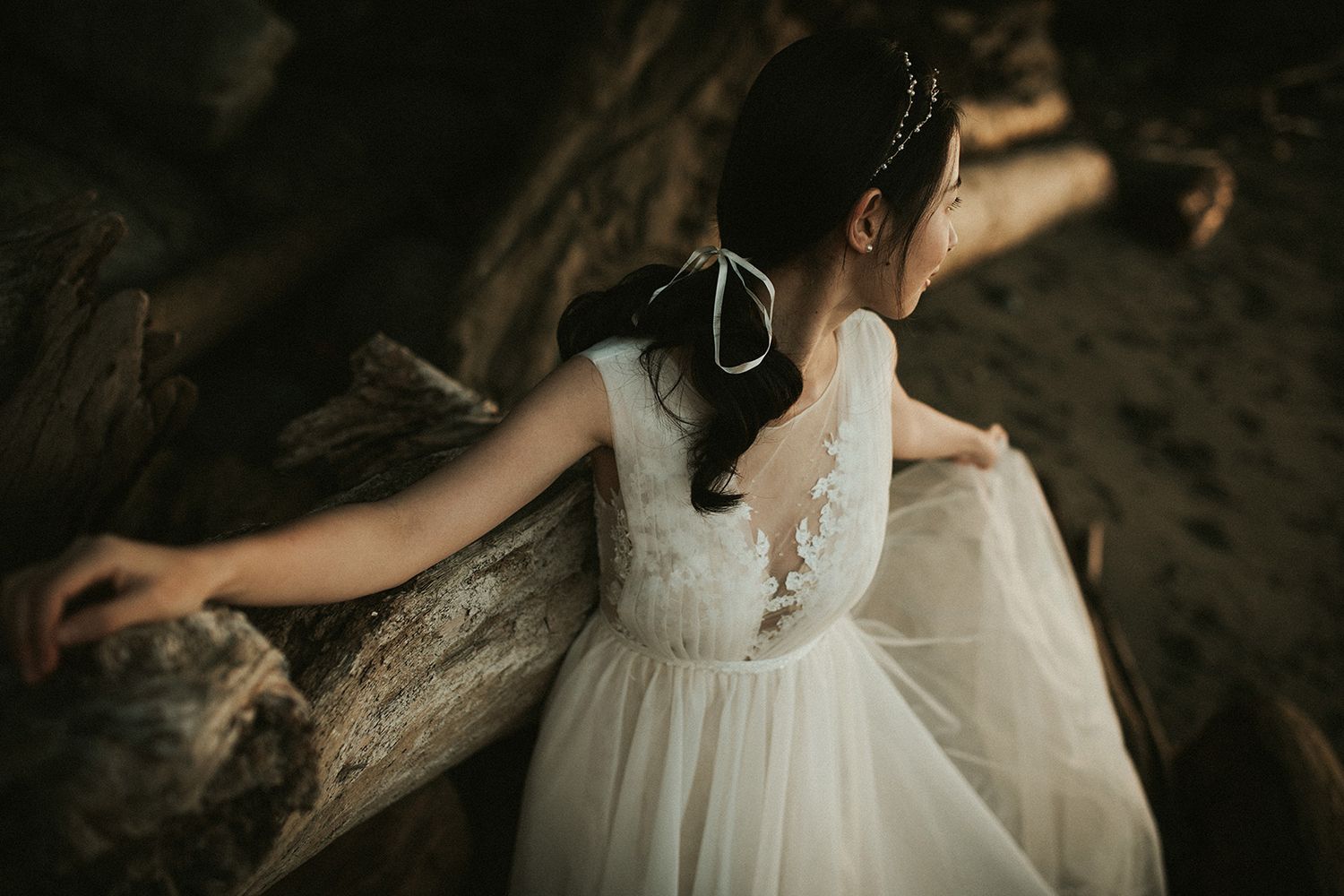 A bride in a white lace wedding dress walks through a dimly lit cave tunnel during a photo session at Spanish Banks beach in Vancouver.