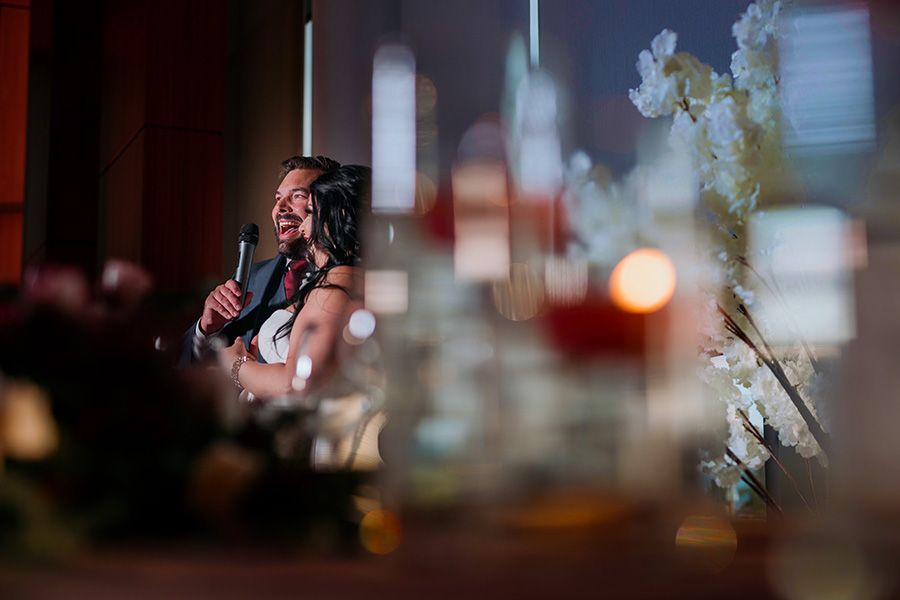 Blurred bokeh lights create a dreamy abstract foreground with warm orange and blue tones while a wedding couple speak at their wedding.
