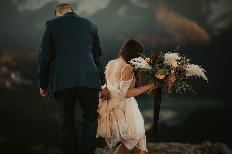 A romantic wedding couple stands silhouetted against a dramatic stormy sky in a moody outdoor setting.