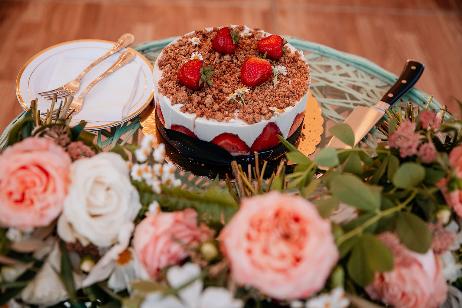 Delicate pink garden roses and white floral arrangements adorn a wedding cake topped with strawberries.