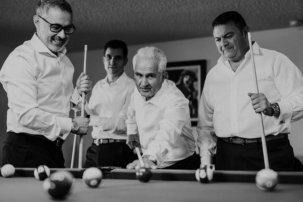 A black and white photo showing people playing billiards and lining up shots at a pool table.