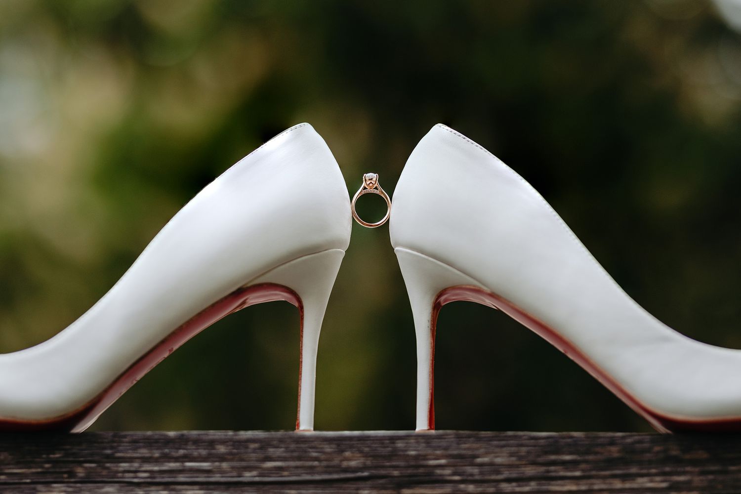 Close-up details of elegant white wedding shoes arranged in an artistic angle with an engagement ring balanced between them.