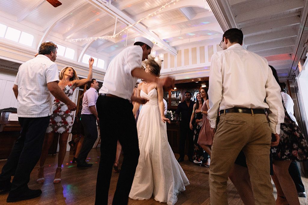 Wedding guests dance together on a crowded dance floor during an evening reception celebration.