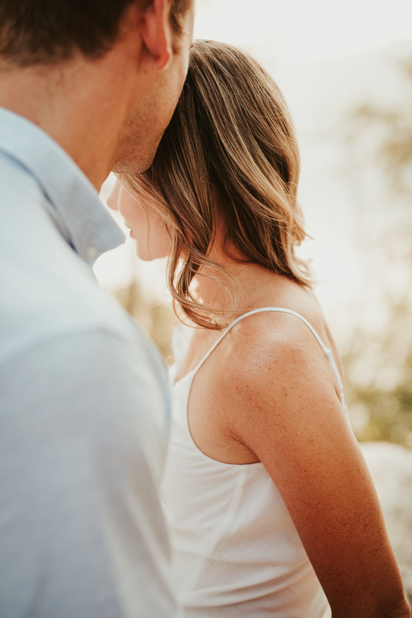 Romantic close-up of a couple in white clothing during a sunset photo shoot with soft golden lighting.