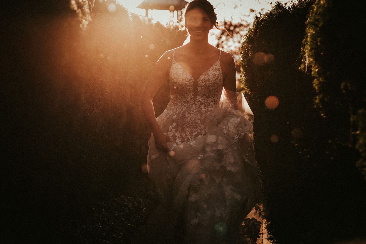 A very happy bride runs toward the camera, her wedding dress floats up around her feet. The low Autumn sun shines behind her.