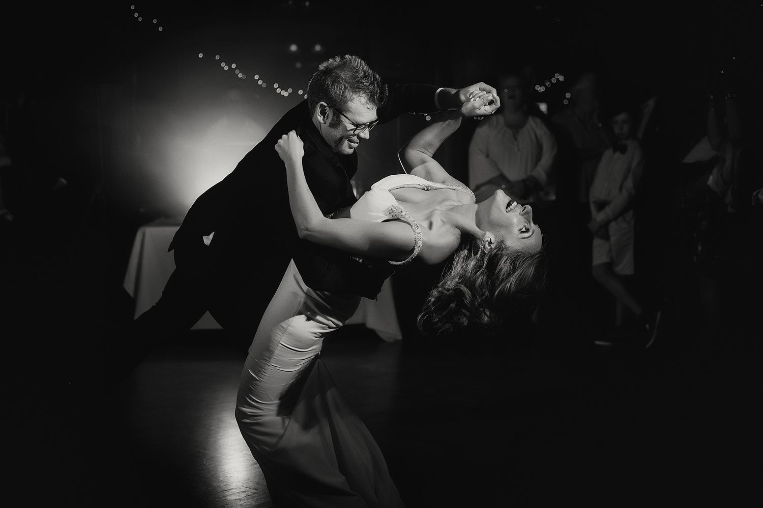 A dramatic black and white dance performance with dancers in close embrace performing tango moves.