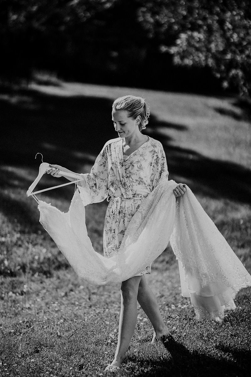 A black and white photo showing a bride-to-be carrying her flowing white wedding dress in natural outdoor lighting.