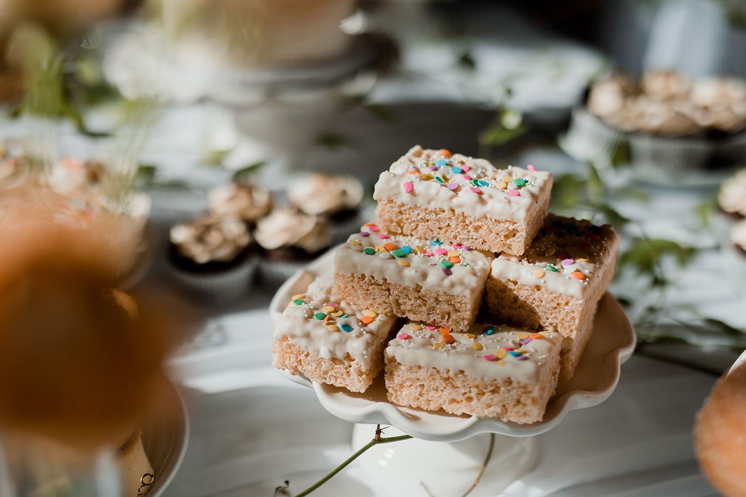 Homemade marshmallow rice krispie treats topped with colourful sprinkles displayed on white serving plates.