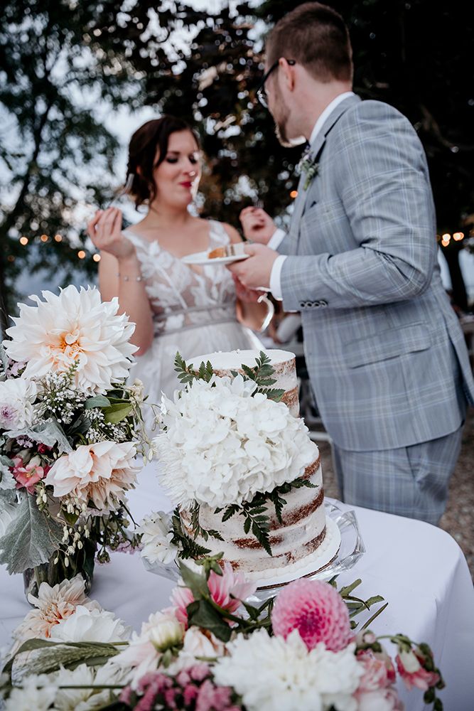 Wedding cake cutting scene with white floral decorations and pink accents at an outdoor reception.
