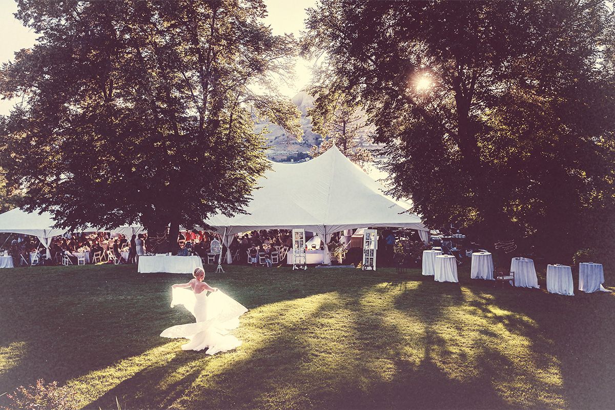 White event tents and vendor booths line a grassy park area during a summer garden wedding reception.