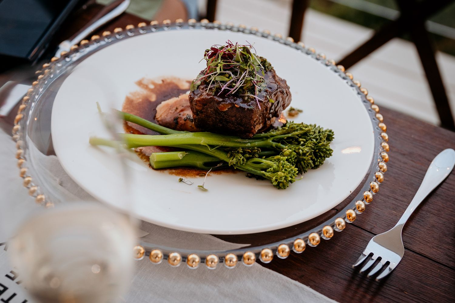 Elegant plated dishes with broccolini and meat served on white plates with decorative gold beaded rims at Vows and Vines Vineyard.
