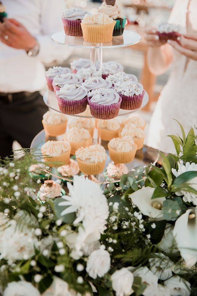 Elegant tiered cupcake display with frosted treats surrounded by white floral arrangements and greenery at an event.