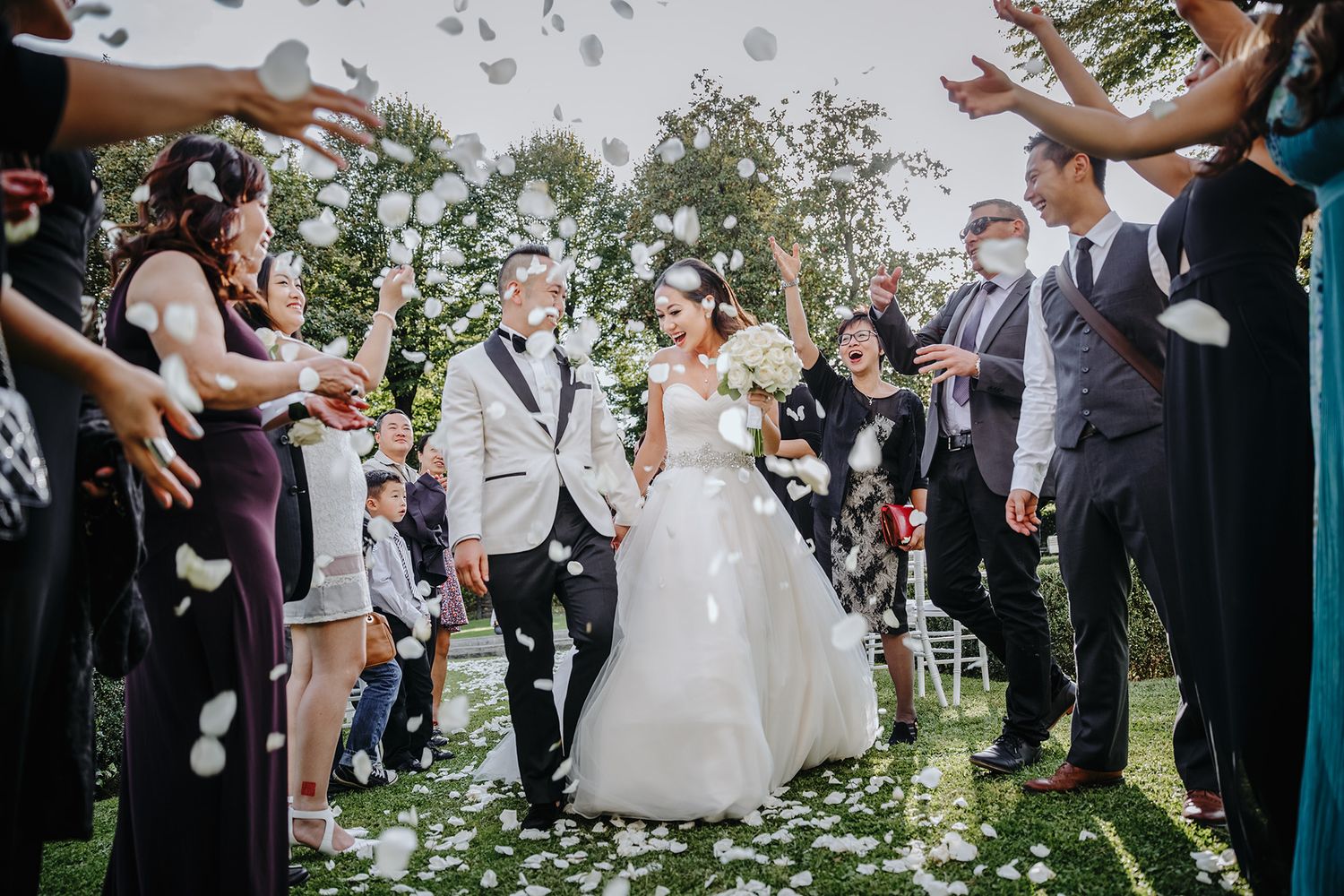 Wedding guests toss rose petals in celebration as a couple exits their outdoor garden ceremony.