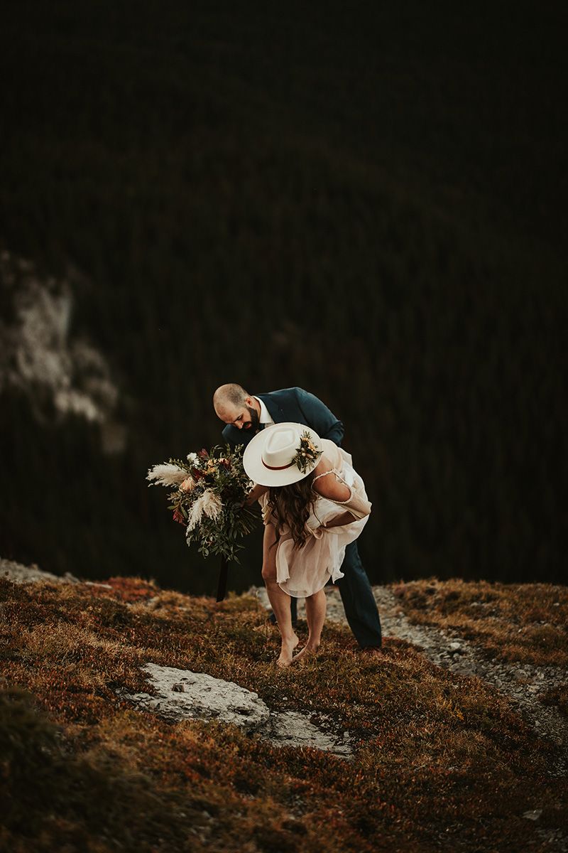 A couple shares an intimate moment on a scenic hillside during a moody sunset photo shoot.