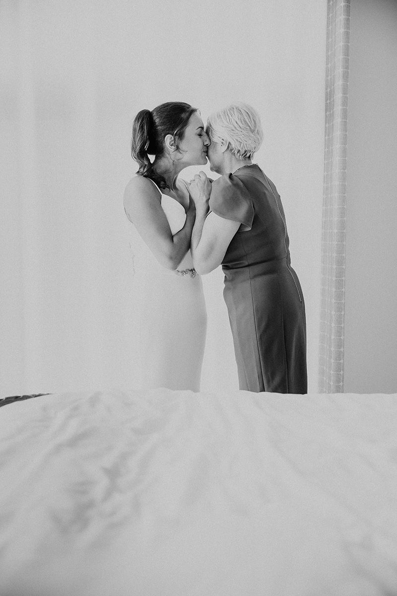 A romantic black and white photo showing a bride and her mom sharing an emotional moment in a bright boudoir.