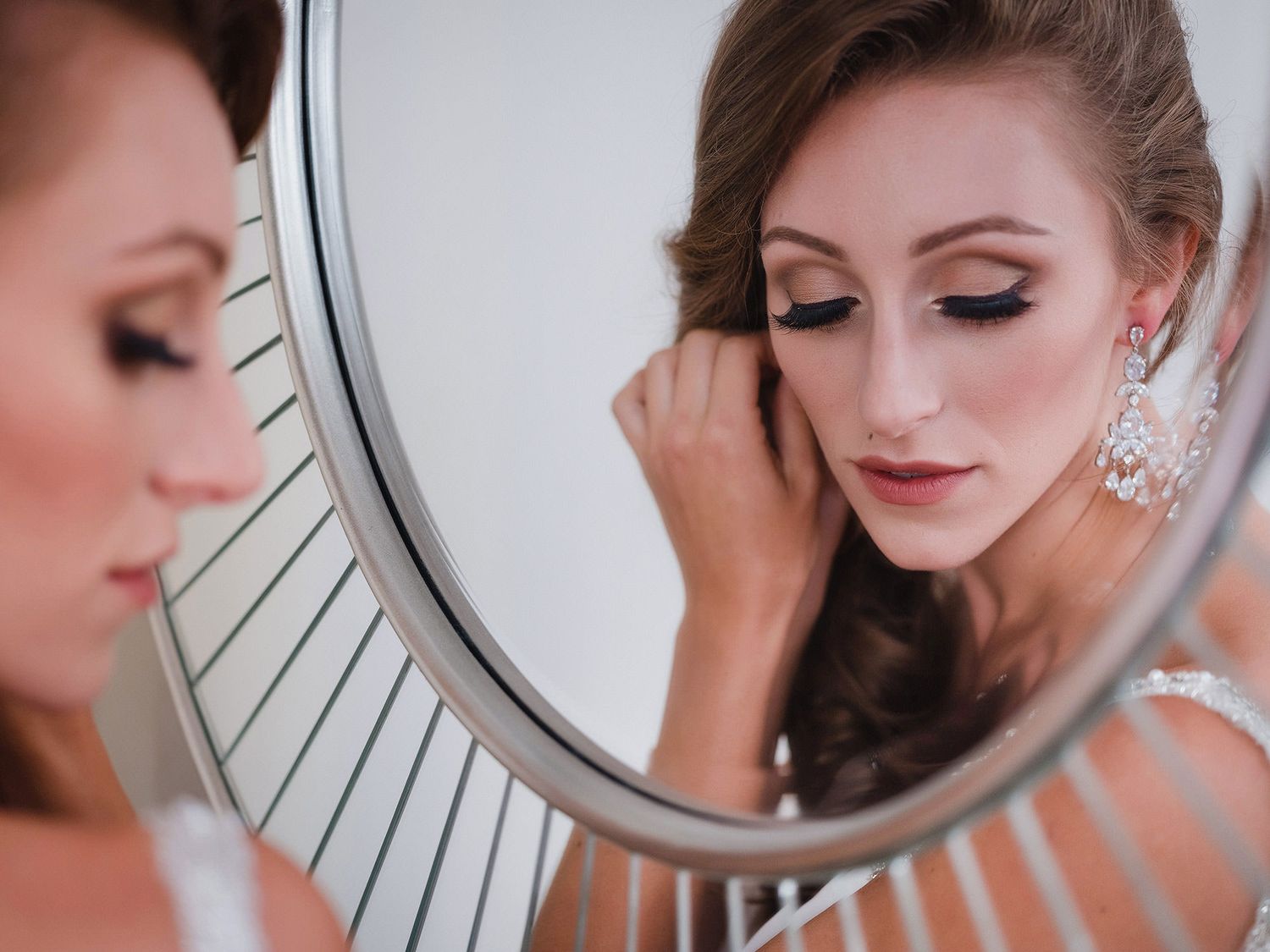 A bride adjusts her earring while looking in a mirror during wedding preparations.