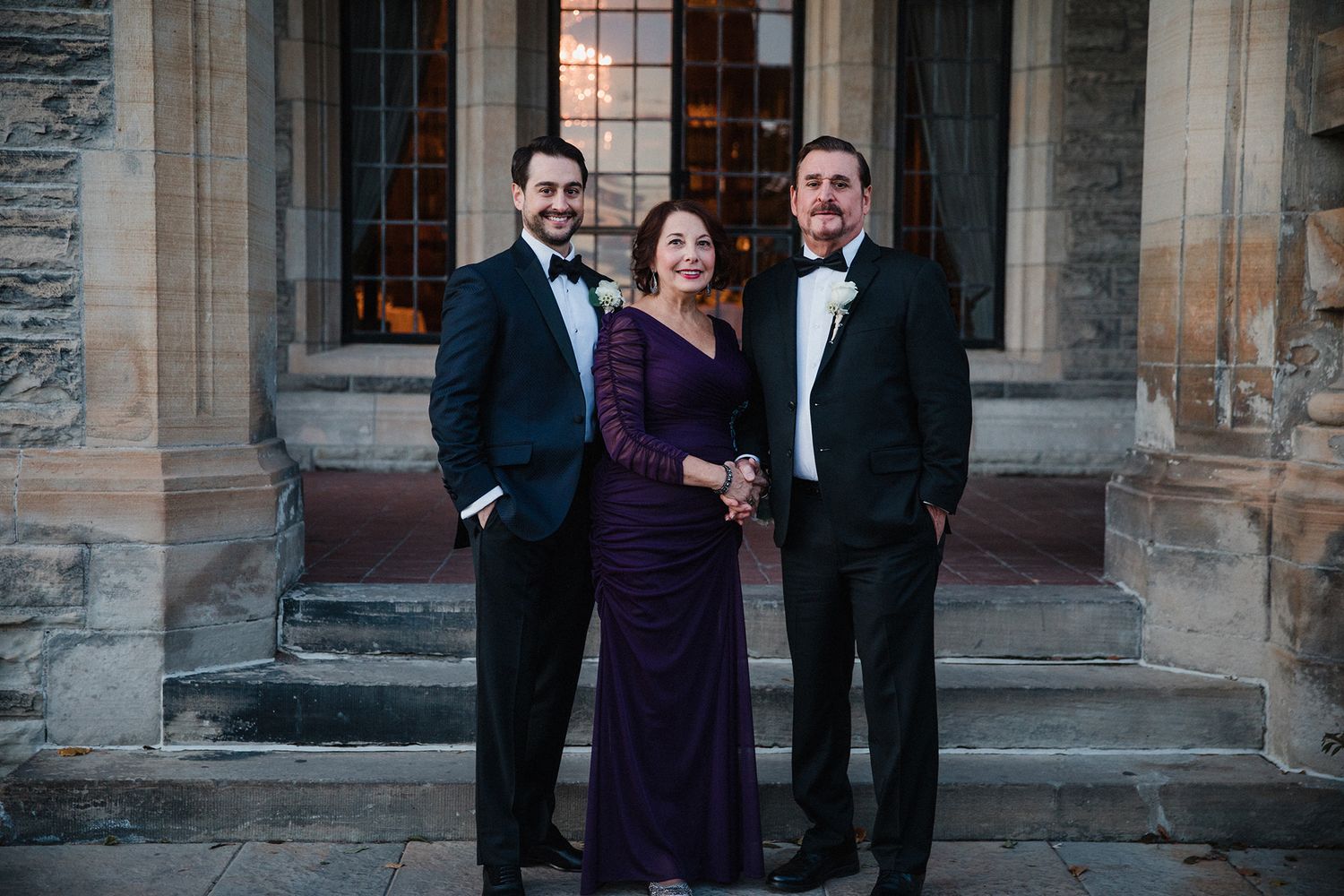 Wedding party members in formal attire pose together on stone steps outside a historic building.