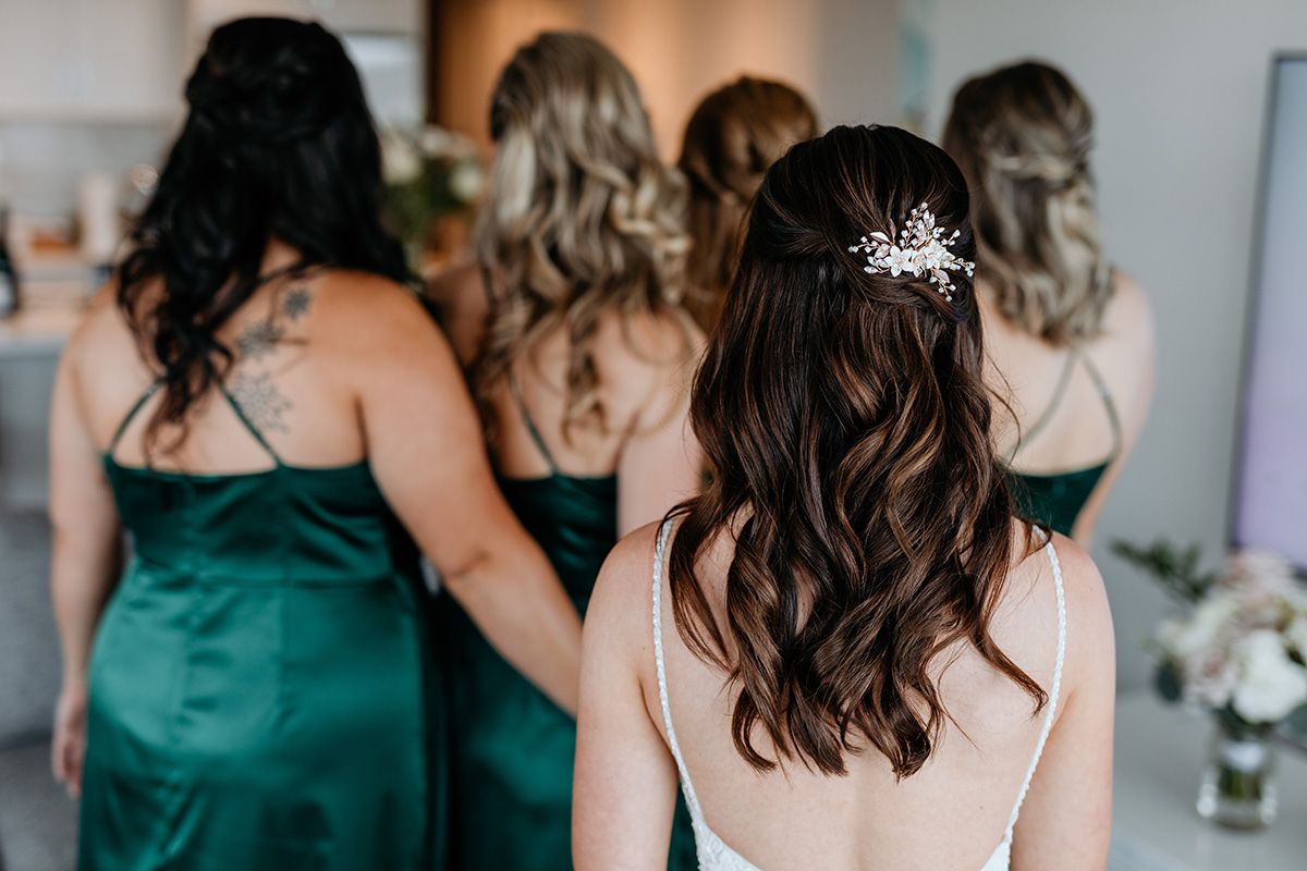 Bridesmaids in emerald green dresses stand together just before the bride in the foreground surprises them.