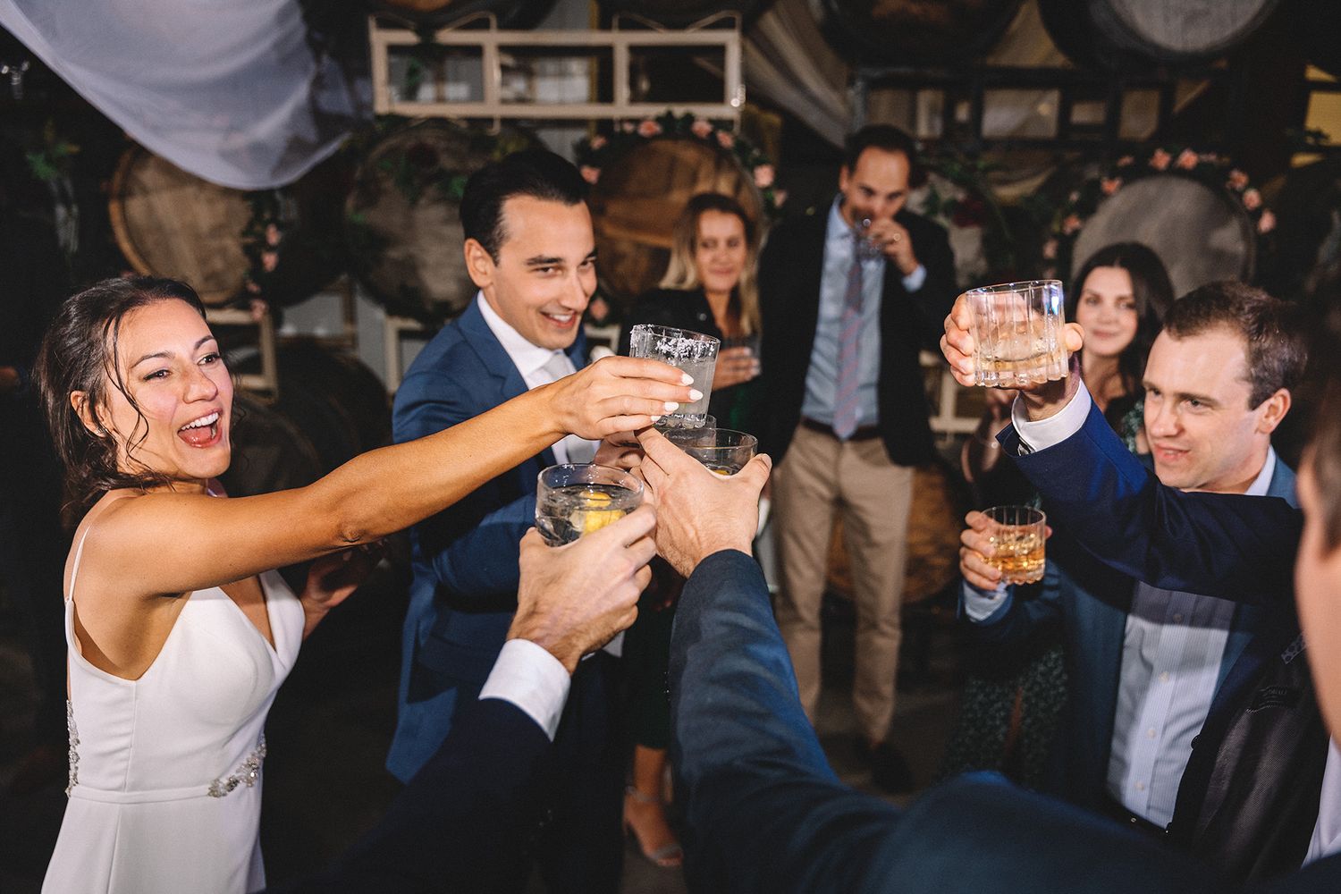 A group of people dancing and celebrating at a lively wedding reception in a dimly lit venue.