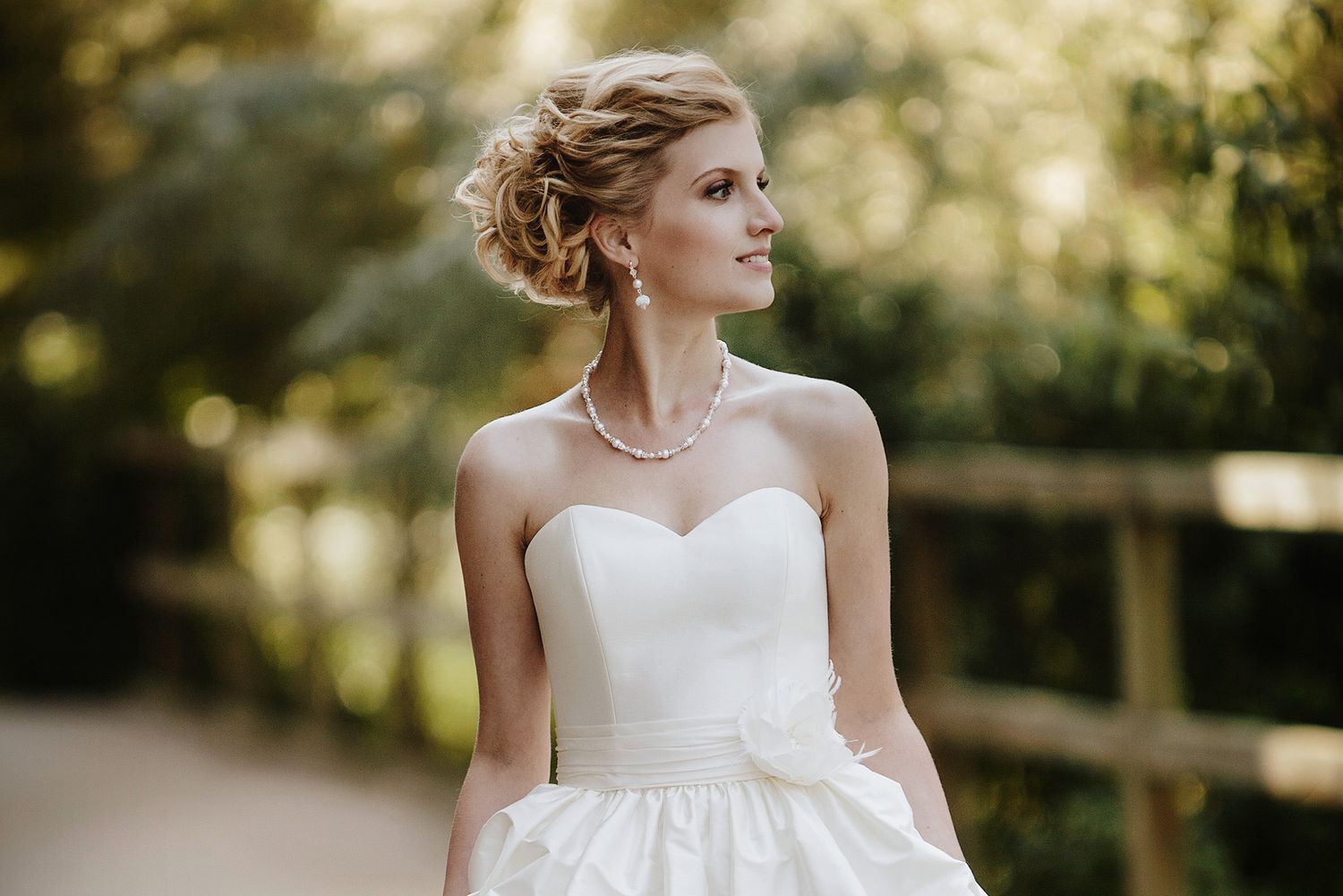 A bride in a white wedding dress poses outdoors in a garden setting with soft natural lighting.