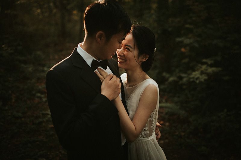 A bride and groom share an intimate moment while dancing together in a romantic forest setting.