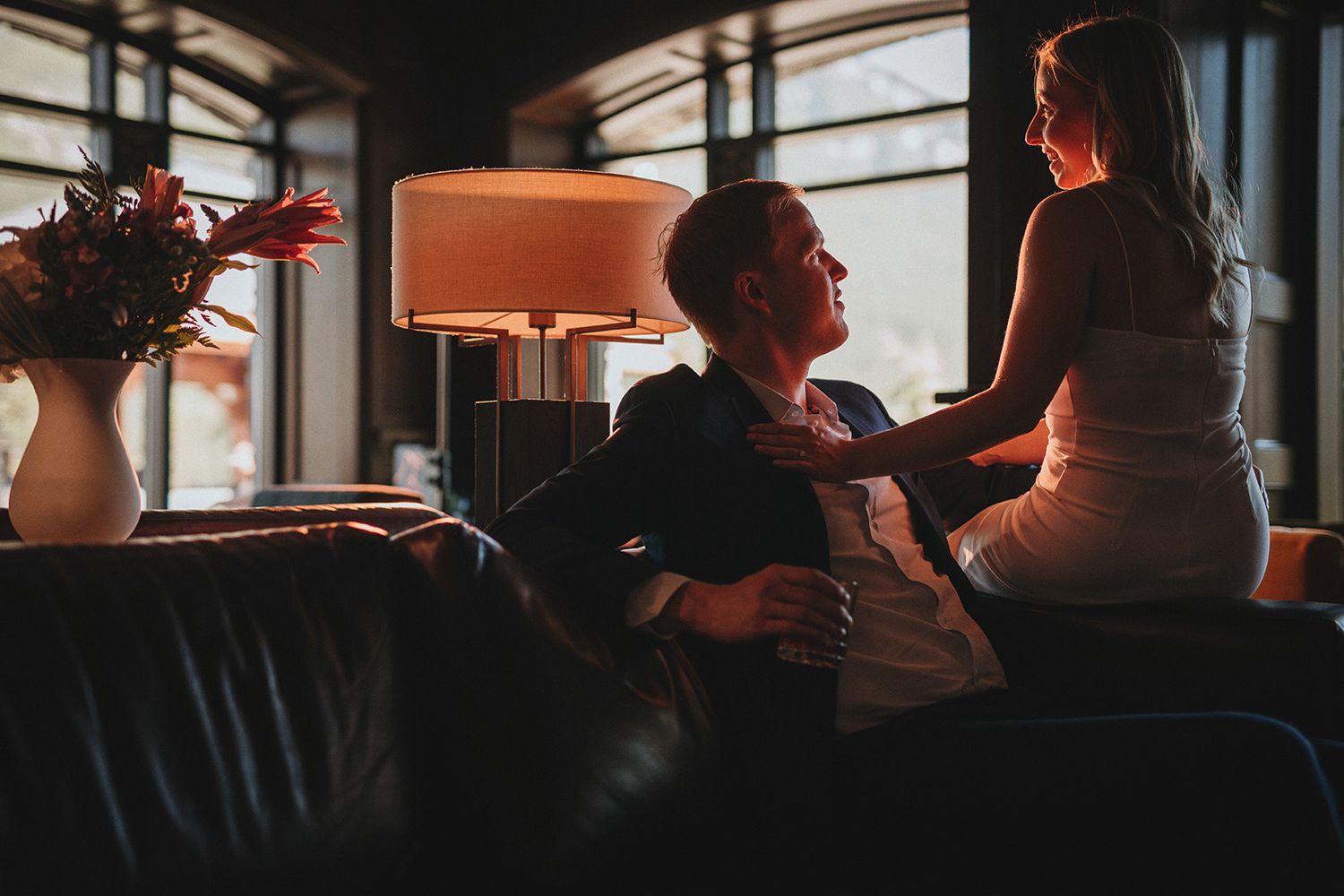 romantic lighting set the mood in this romantic photo of a couple sitting on a leather sofa with window and lamp light.
