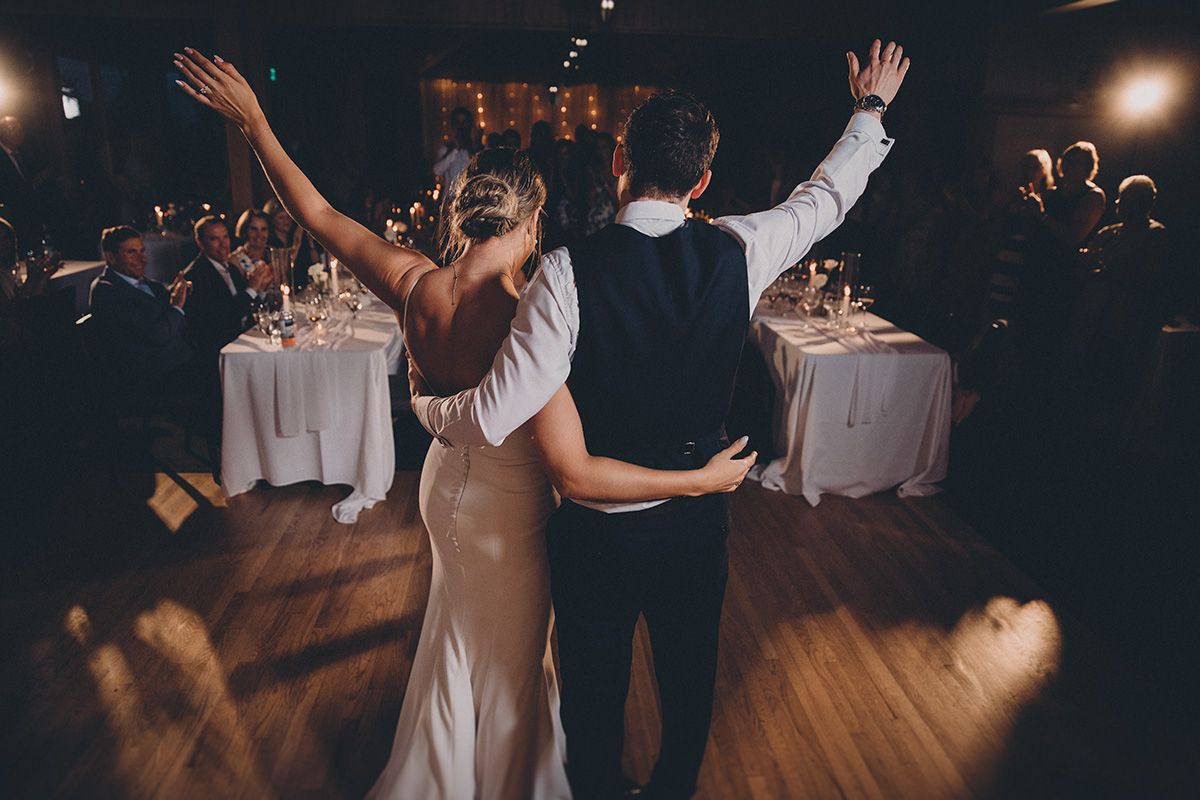 Wedding guests dance together on a dimly lit wooden dance floor during a reception celebration.