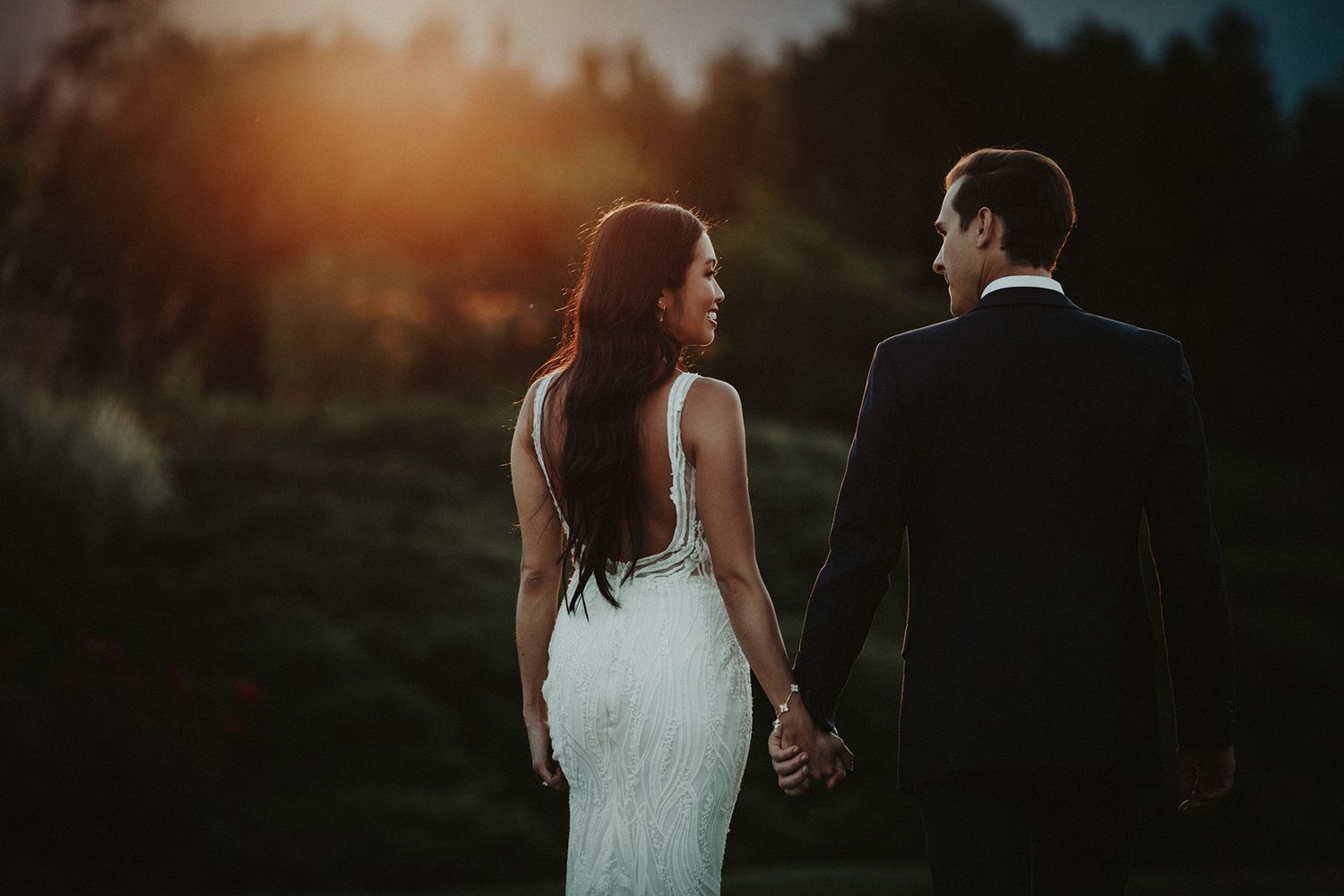 A wedding couple walking together at sunset in a romantic outdoor setting with golden light filtering through trees. The Harvest Golf Club.