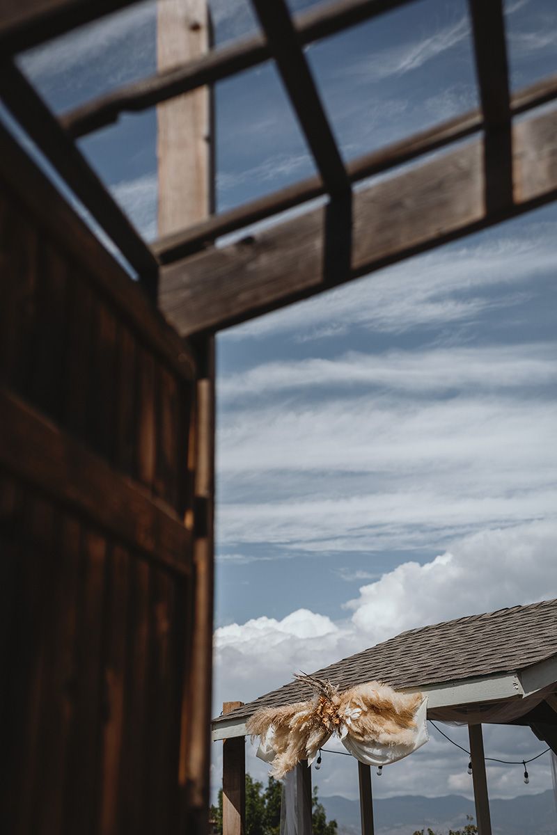 A wooden pergola frames a scenic mountain view against a cloudy blue sky.
