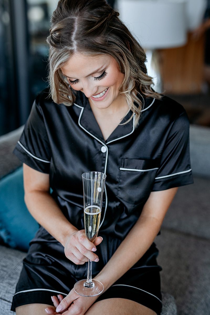 Woman in black silk pajamas relaxes with champagne in elegant lifestyle photoshoot series.