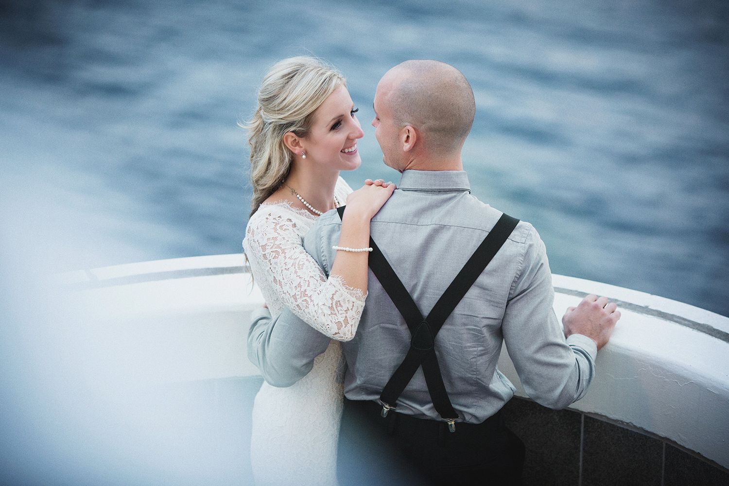 A romantic couple shares intimate moments during their wedding photo shoot on a boat against a dreamy blue-water background.