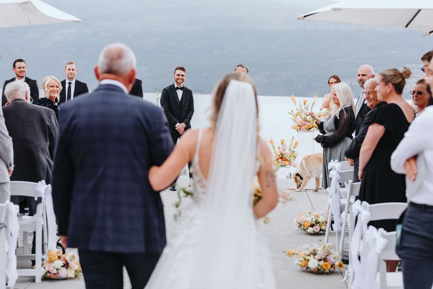 A groom looks on with anticipation as a bride and her father walk the aisle at their wedding at 50th Parallel Winery.