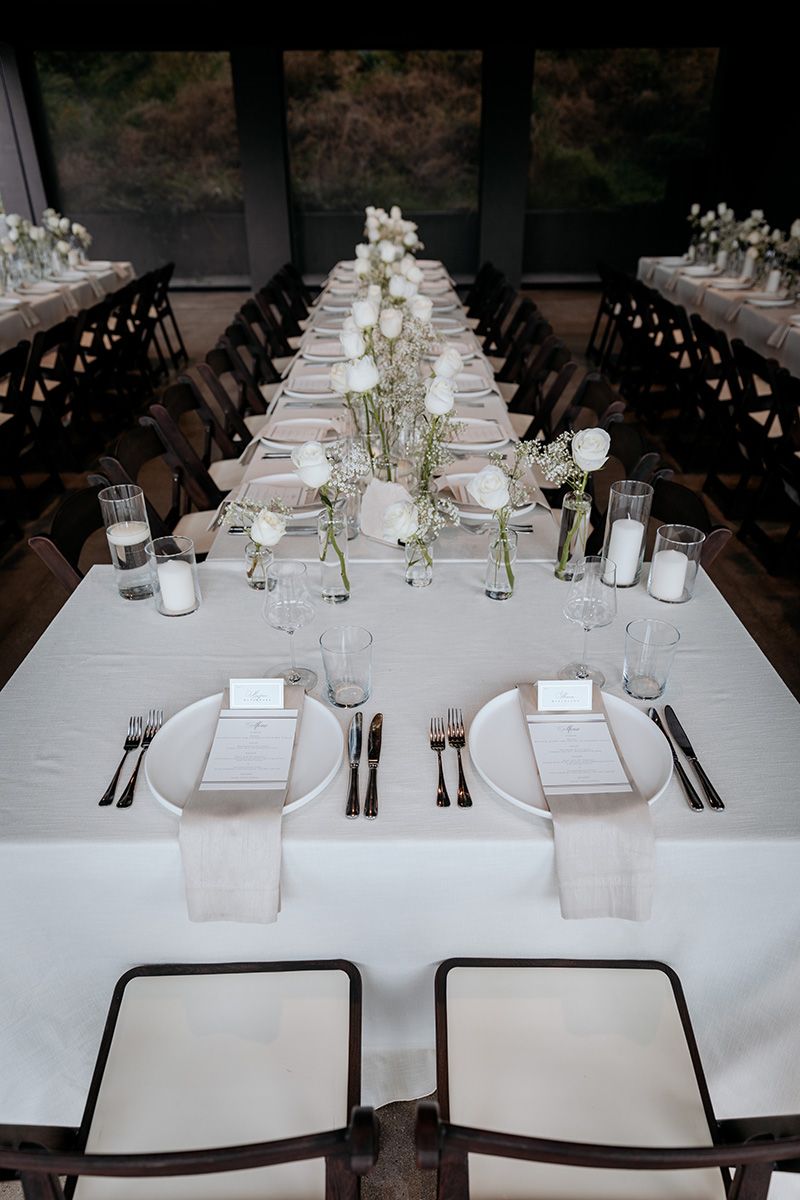 Elegant wedding reception tables set with white linens, place settings, and delicate floral center-pieces in a modern venue.