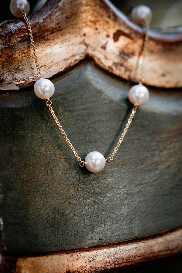A delicate pearl necklace with gold chain links shown in multiple close-up angles against a dark textured surface.