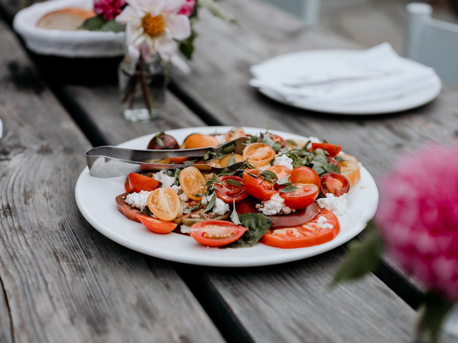 Fresh tomato and asparagus salad with shrimp served on white plates with colourful flowers in the background.