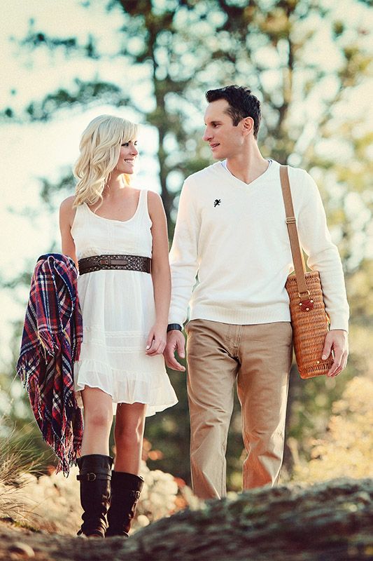 A romantic couple walking together in nature wearing casual white and tan outfits with a plaid accent piece.
