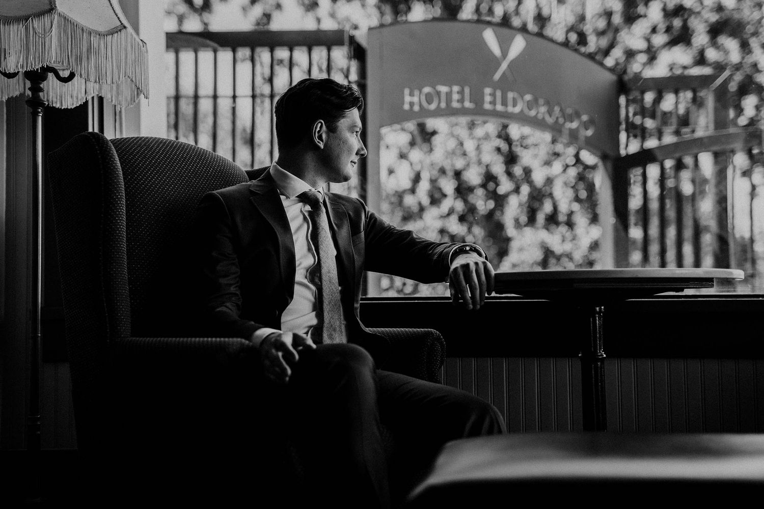 A black and white photo of a groom looking out the window of the Hotel Eldorado bar moments before his wedding.