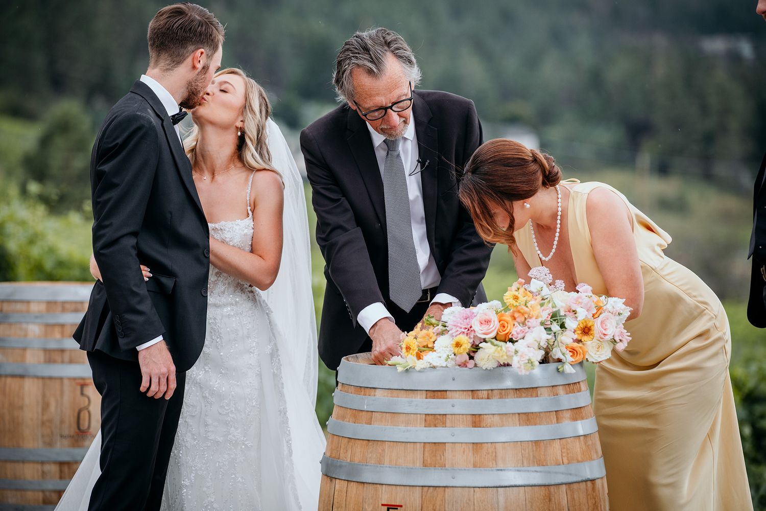 Wedding couple shares romantic moments around rustic wine barrels at an outdoor vineyard celebration.