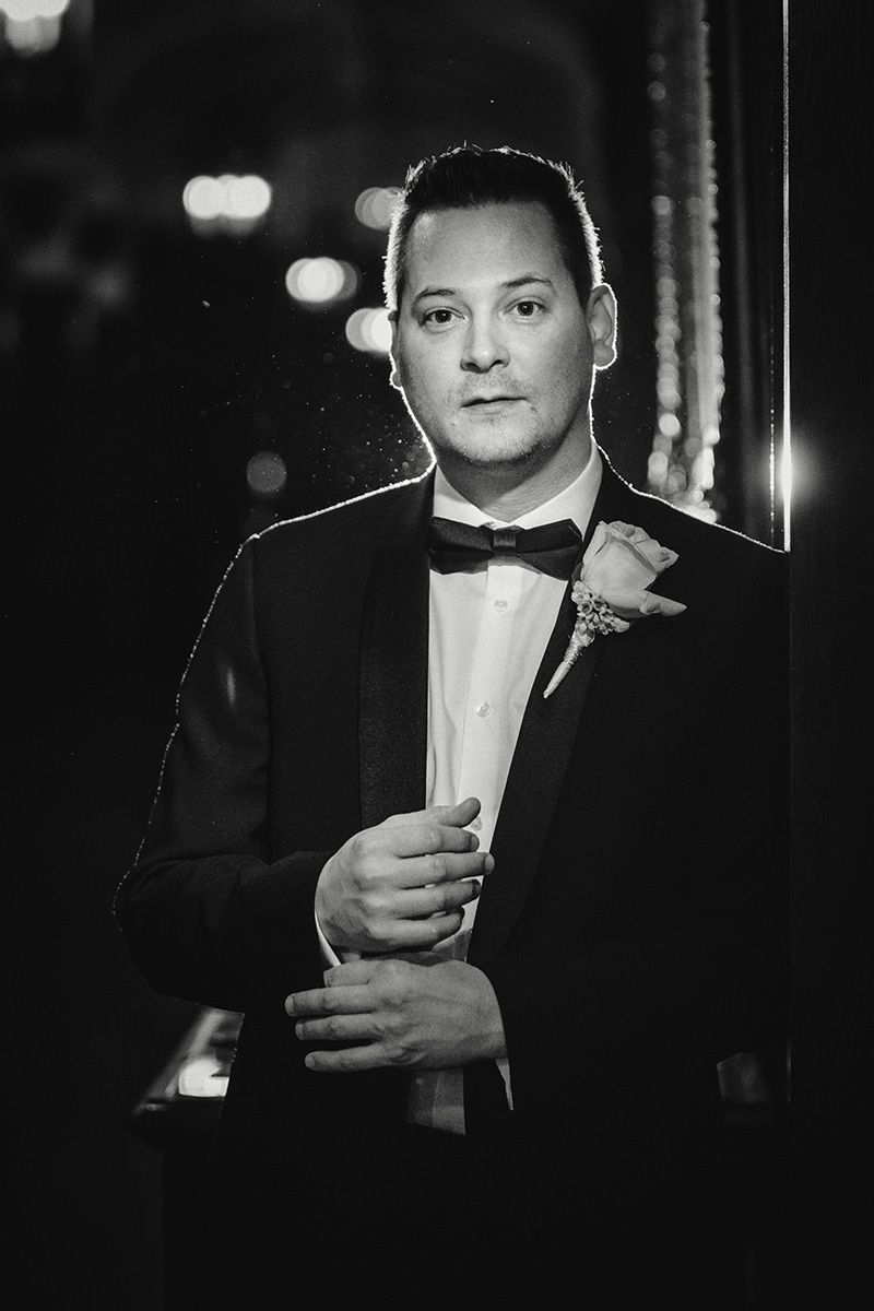 A black and white photo showing a man in formal attire drinking from a glass in dramatic lighting.