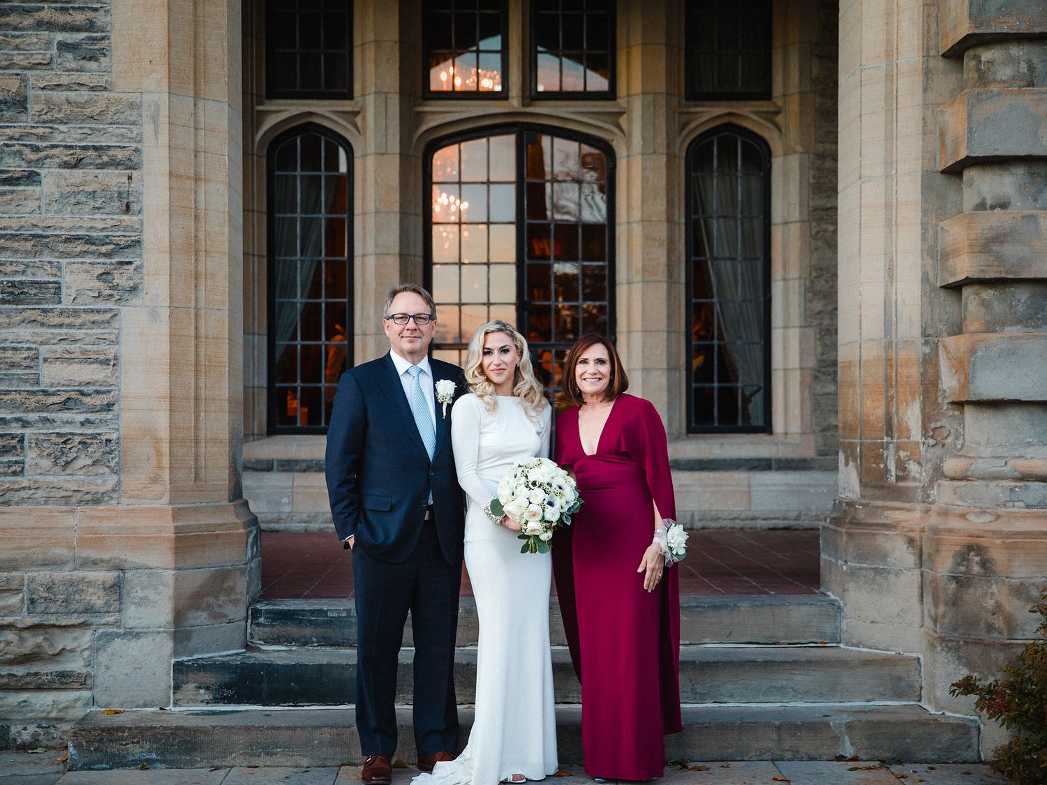 Wedding party members stand outside a historic stone church building in formal attire.