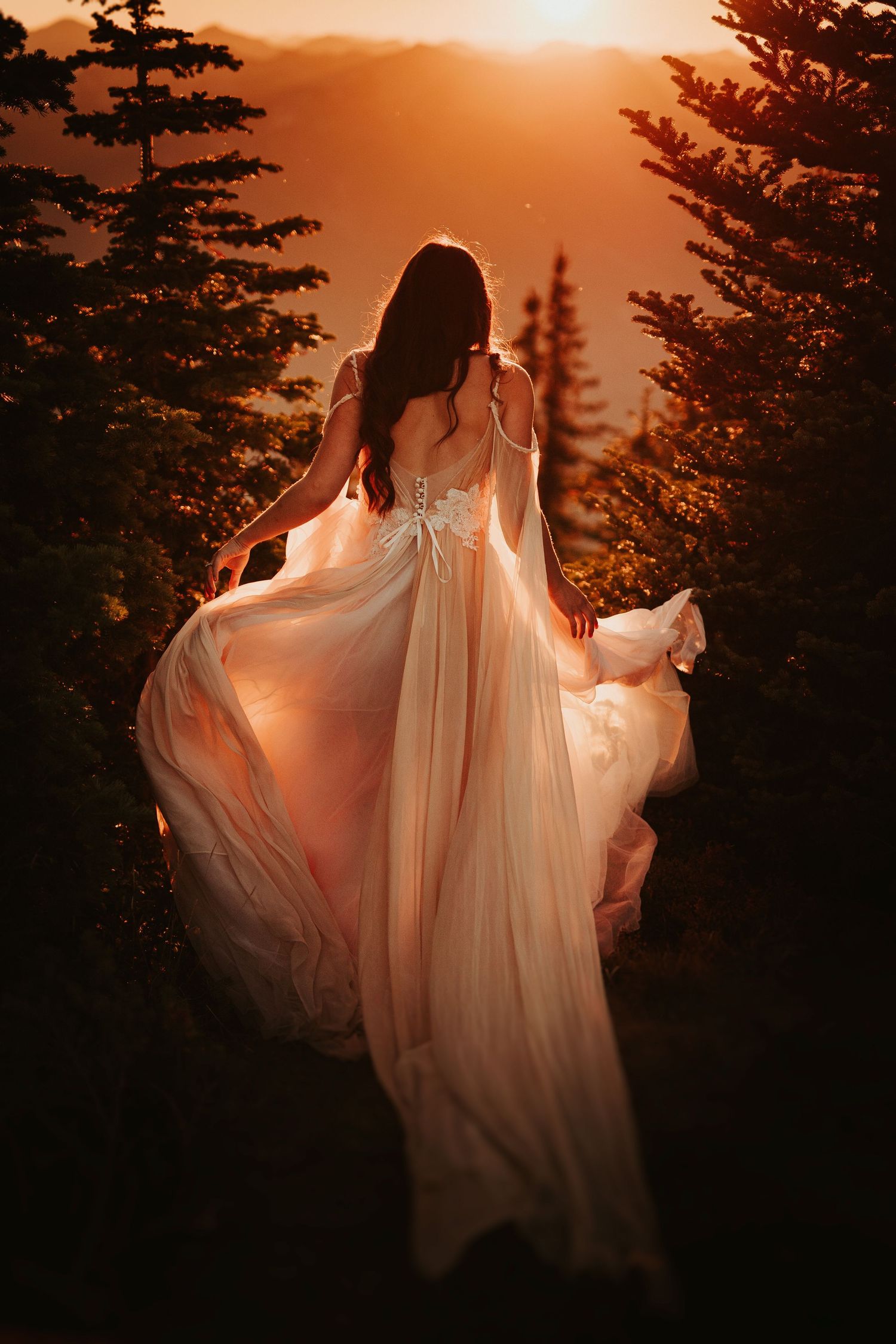 Ethereal bride in flowing white dress silhouetted against dramatic sunset in pine forest.
